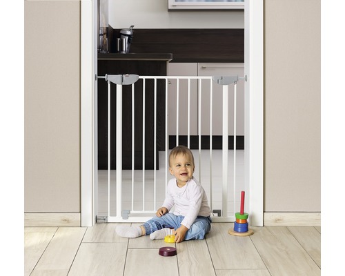 Kind sitzt vor einem weißen Schutzgitter im Türrahmen