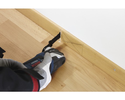 Eine Person benutzt einen Multifunktionsschneider an einer Holzfußleiste, um einen präzisen Schnitt durchzuführen.