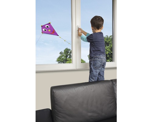 Junge betätigt einen Fenstergriff, während draußen ein Drachen fliegt.