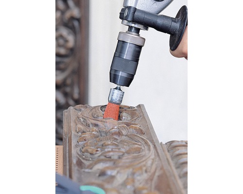 Bohrmaschine mit Bürstenaufsatz reinigt ein Holzornament
