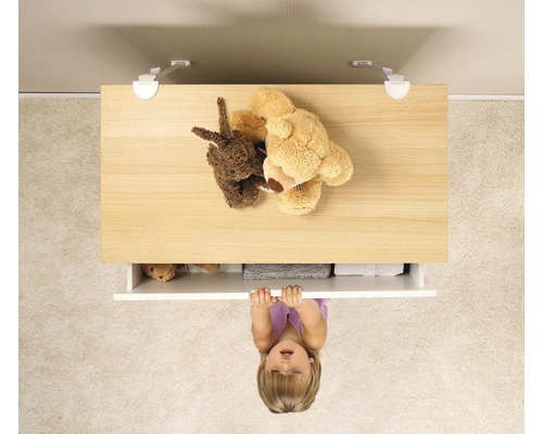 Kind zieht an einer Kommode mit Kindersicherung, auf der Teddybären liegen