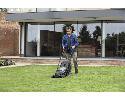 Mann mäht Rasen mit einem Rasenmäher im Garten vor dem Haus.