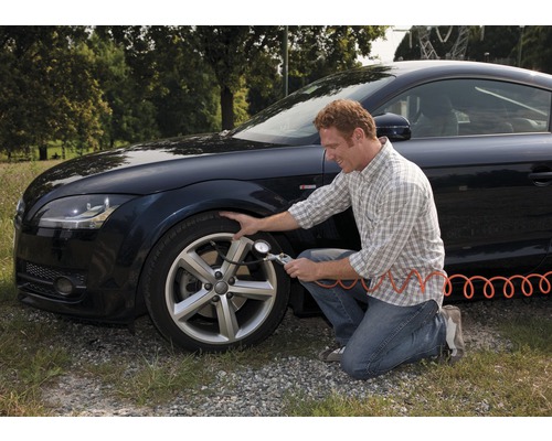 Mann überprüft Reifendruck am Auto mit einem Reifendruckmesser