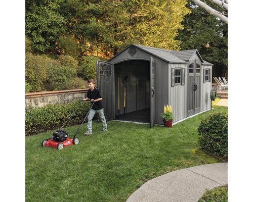 Gartenszene mit Gerätehaus und Person beim Rasenmähen