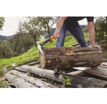 Ein Mann spaltet mit einer Spaltaxt einen Holzstamm im Freien.