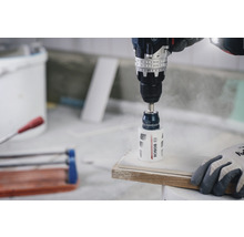 Eine Bohrmaschine bohrt mit einem Lochsägen-Aufsatz ein Loch in ein Werkstück.