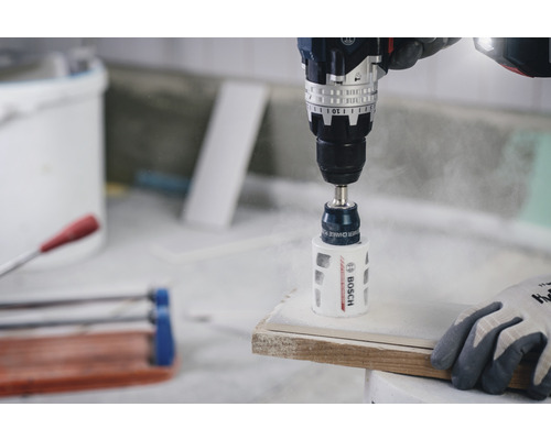 Eine Bohrmaschine bohrt mit einem Lochsägen-Aufsatz ein Loch in ein Werkstück.