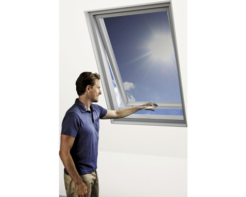 Ein Mann öffnet ein Dachfenster und blickt in den blauen Himmel.
