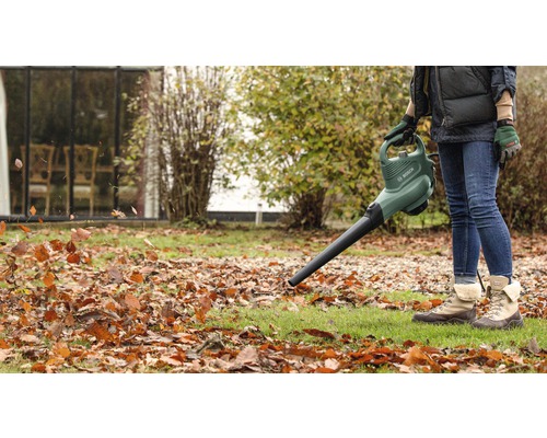 Eine Person benutzt einen Laubbläser im Garten, um Laub zu entfernen.