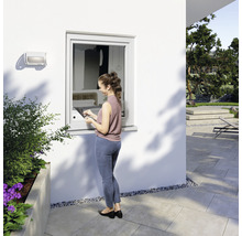 Frau bedient Fenster mit Tablet im Aussenbereich eines Hauses.