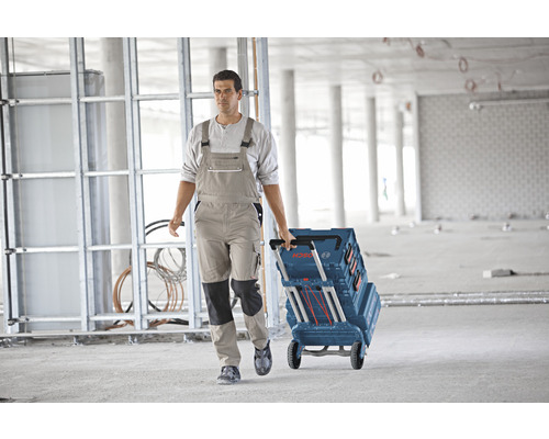 Handwerker zieht einen Werkzeugkoffer mit Rollen von Bosch durch einen Rohbau.