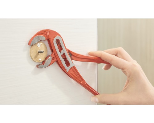 Eine Person benutzt eine Rohrzange, um einen Holzdübel mit Schraube in eine weiße Oberfläche zu drehen.