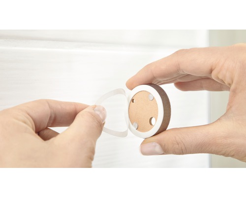 Eine Hand entfernt die Schutzfolie von einem runden Möbelknopf zur Montage.