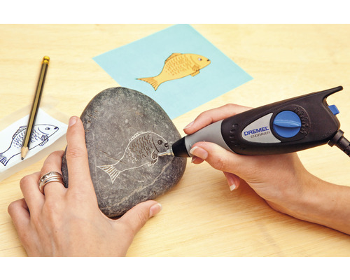 Eine Person graviert mit einem Dremel Graviergerät ein Fischmuster in einen Stein.