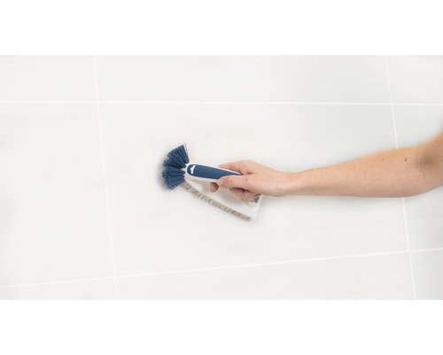 Eine Hand hält eine Bürste zum Reinigen von Fliesenfugen.