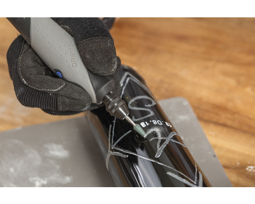 Eine Person graviert mit einem Dremel Gerät eine dunkle Flasche.