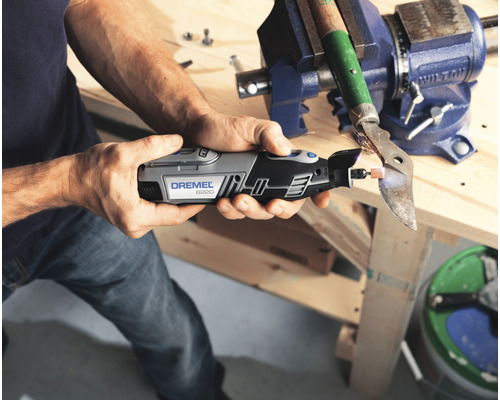 Mann schleift Metall mit einem Dremel Multifunktionswerkzeug, das in einem Schraubstock befestigt ist