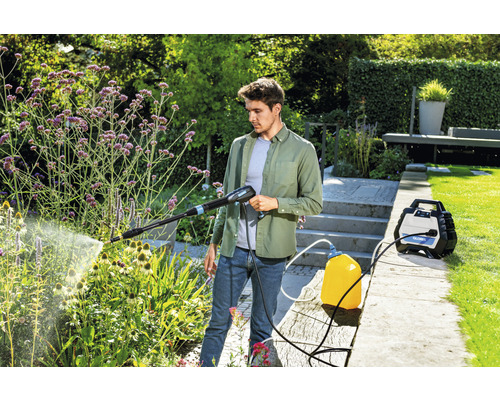 Mann benutzt einen Hochdruckreiniger im Garten zur Pflanzenbewässerung