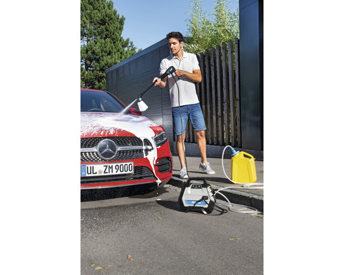 Ein Mann reinigt ein Auto mit einem Hochdruckreiniger, während ein gelber Wasserkanister und das zugehörige Gerät daneben stehen.