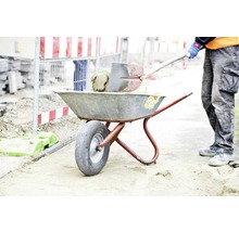 Bauarbeiter befüllt Schubkarre mit Schaufel auf Baustelle
