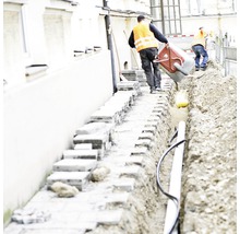 Bauarbeiter arbeiten an einem Graben mit Rohren und Pflastersteinen.