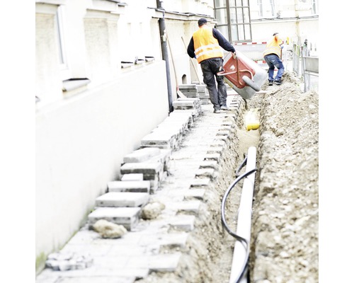 Bauarbeiter arbeiten an einem Graben mit Rohren und Pflastersteinen.