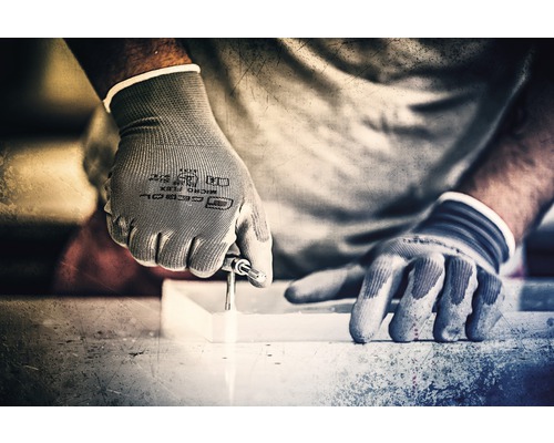Eine Person bohrt mit Handschuhen ein Loch in ein Werkstück.