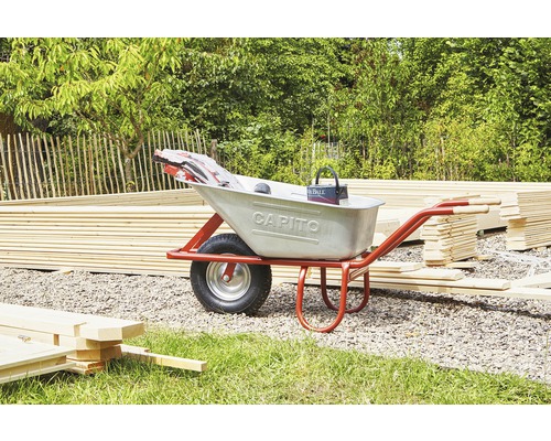 Eine Schubkarre mit Baumaterial und Werkzeugen in einem Garten.