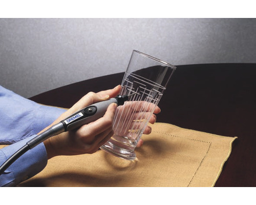 Eine Person graviert mit einem Graviergerät ein Glas mit einem Linienmuster.