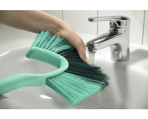 Hand unter Wasserhahn mit Reinigungsbürste im Waschbecken