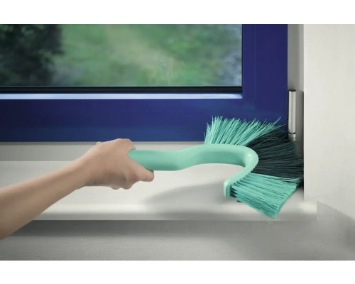 Eine Hand reinigt mit einer Fensterrahmbürste einen Fensterrahmen.