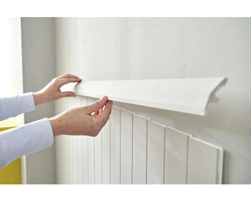 Person montiert eine weiße Zierleiste an einer Wand mit Paneelen