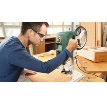 Ein Mann bedient eine Tischbohrmaschine in einer Werkstatt.