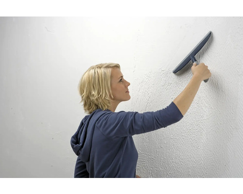 Frau glättet Putz an einer Wand mit einer Glättkelle