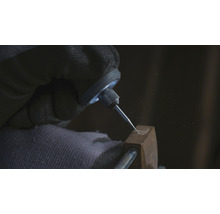 Detailaufnahme einer Hand mit Schutzhandschuh, die mit einem Gravierstichel in ein Metallobjekt eine Form graviert