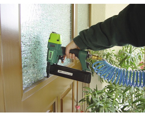 Eine Person befestigt mit einem Druckluftnagler eine Leiste an einem Fensterrahmen.