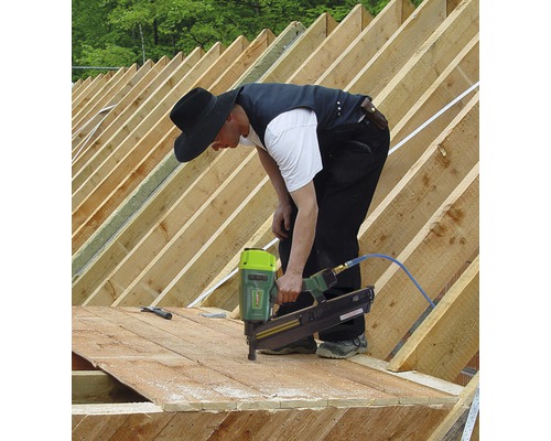 Handwerker befestigt Holz auf einem Dachstuhl mit einem Druckluftnagler