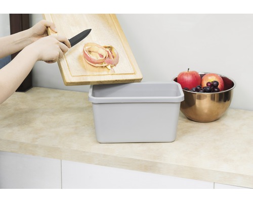 "Eine Person entsorgt Apfelschalen von einem Holzbrett in einen Abfallbehälter