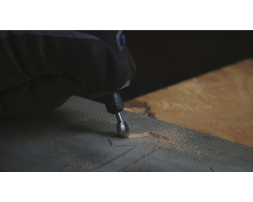 Eine Person graviert mit einem Multifunktionswerkzeug ein Muster in ein Holzbrett.