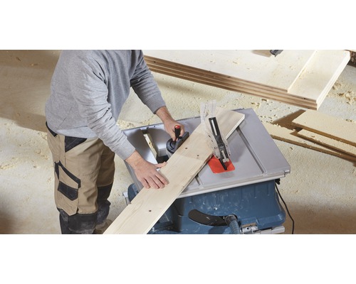 Eine Person schneidet ein Holzbrett mit einer Tischkreissäge.