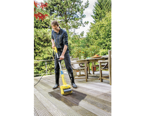 Mann reinigt eine Holzterrasse mit einem Terrassenreiniger.
