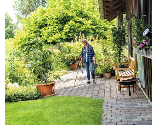 Frau verwendet Unkrautvernichter auf Pflastersteinen im Garten.