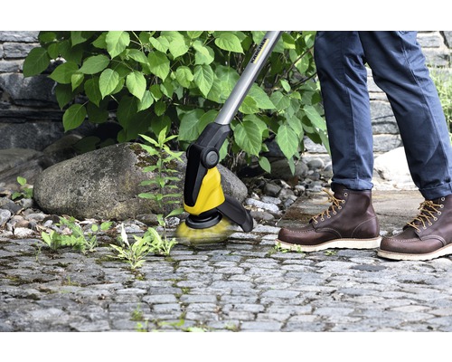 Person entfernt Unkraut mit einer Kärcher Bürste von Pflastersteinen