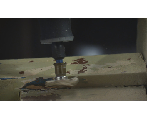 Eine Bohrmaschine schleift Farbe von einem Fensterrahmen.