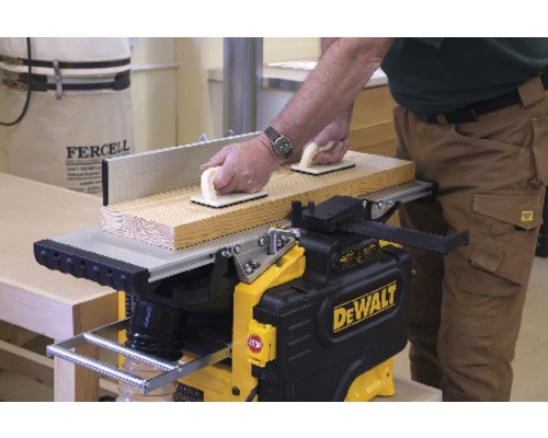 Eine Hobelmaschine mit einem Mann, der ein Holzbrett mit Griffblöcken führt.