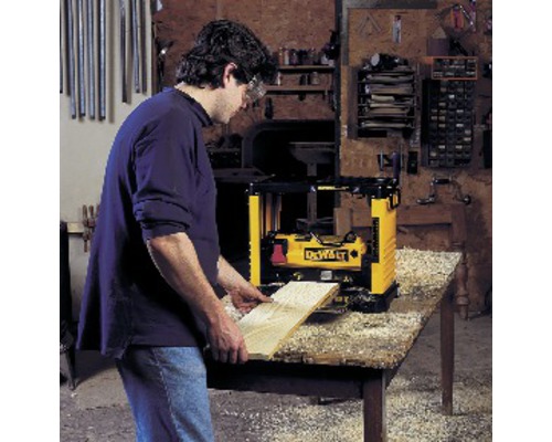 Mann hobelt ein Holzbrett mit einer Hobelmaschine der Marke DeWalt auf einem Tisch.