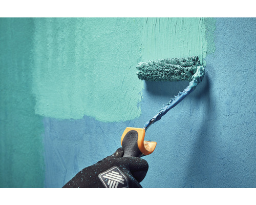 Eine Person streicht mit einer Farbrolle eine Wand.