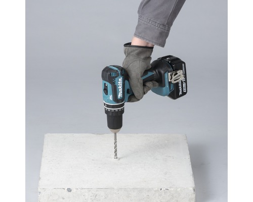 Eine Hand mit Handschuh bohrt mit einem Akku-Bohrschrauber ein Loch in einen Betonblock.