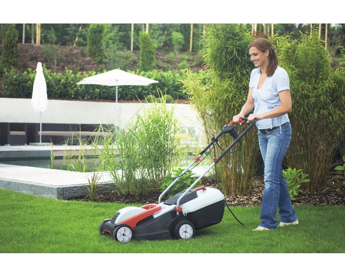 Frau benutzt einen Rasenmäher im Garten.