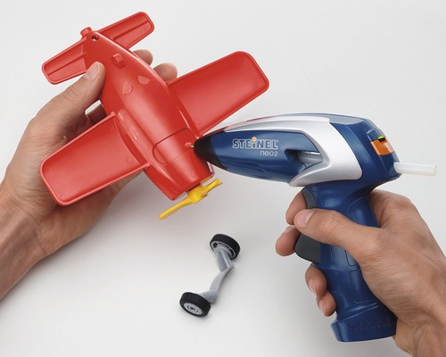 Person klebt ein rotes Spielzeugflugzeug mit einer Heißklebepistole zusammen